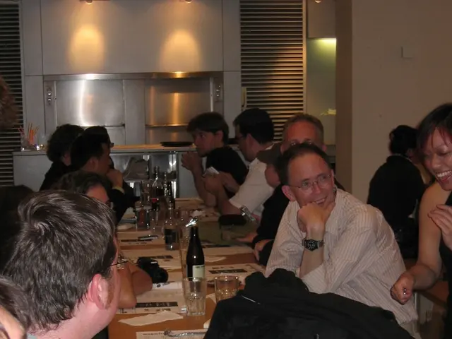 People are sitting on either side of a long table at a party.