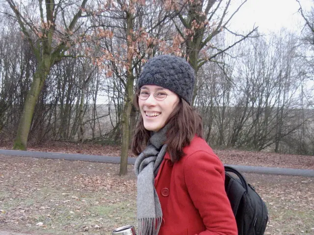 In the image there is a lady in red sweatshirt and scarf with a cap over her head and holding a bag...